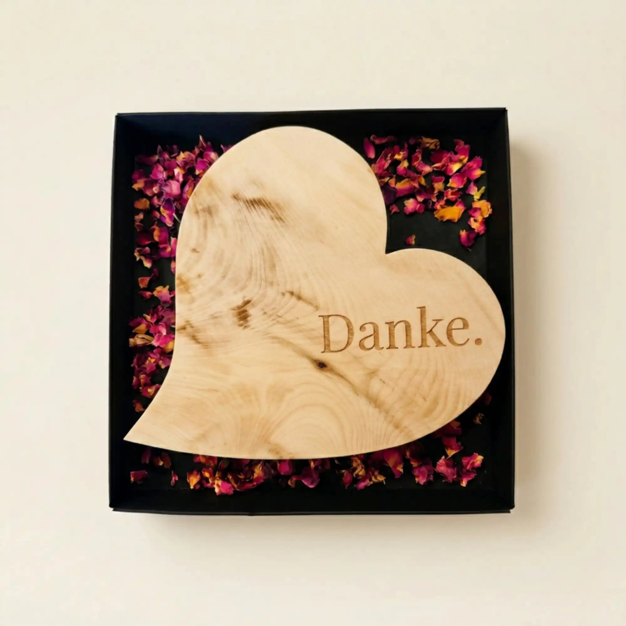 Schlichtes Zirbenholzherz mit der Gravur Danke in einer offenen schwarzen Geschenkbox mit Rosenblueten als Muttertagsgeschenk. Schlichtes Zirbenholzherz mit der Gravur Danke in einer offenen schwarzen Geschenkbox mit Rosenblueten als Muttertagsgeschenk.