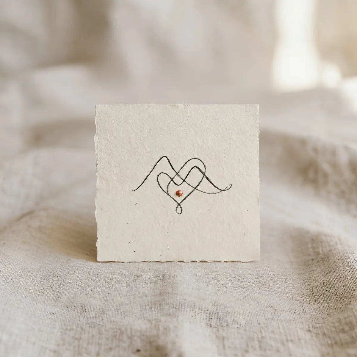 Zwei ineinandergreifende Berg-Herzen als Single‑Line‑Zeichnung auf beigem, handgeschoepftem Papier.