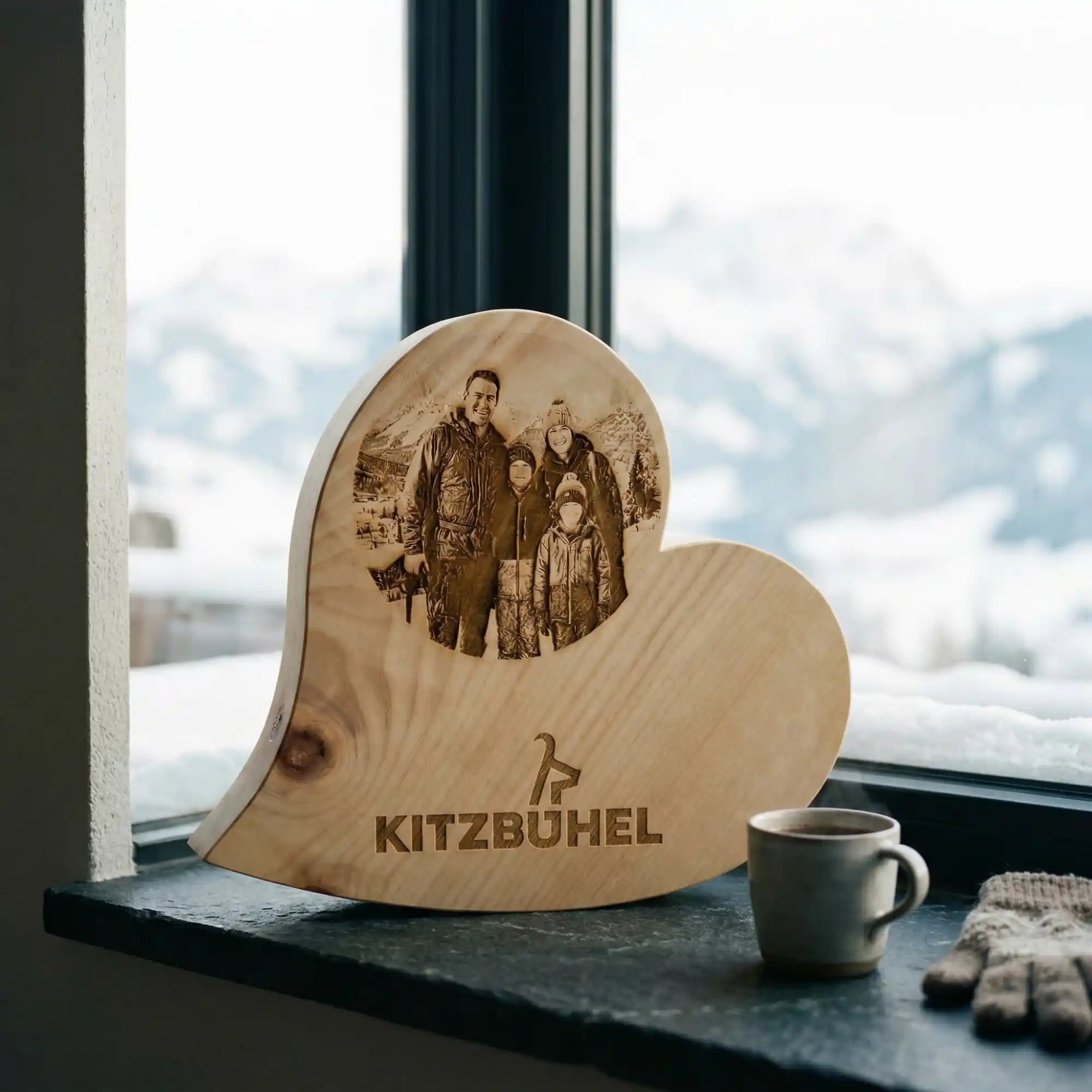 Personalisiertes Zirbenherz mit Kitzbuehel Schriftzug und Familienfoto auf einer Schiefer Fensterbank vor verschneitem Bergpanorama. Personalisiertes Zirbenherz mit Kitzbuehel Schriftzug und Familienfoto auf einer Schiefer Fensterbank vor verschneitem Bergpanorama.