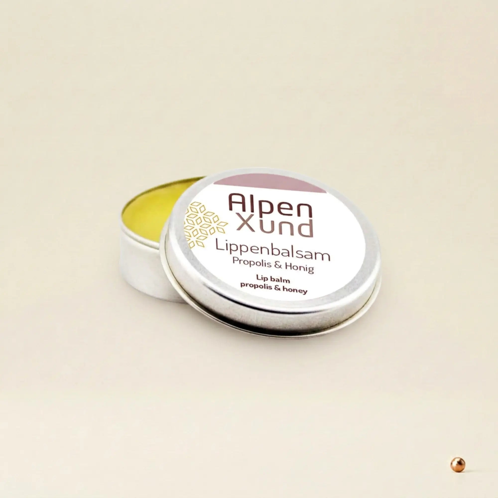 Silberne Lippenbalsam Dose mit Propolis und Honig auf beigem Hintergrund. Flacher Metalltiegel mit weissem Etikett. Silberne Lippenbalsam Dose mit Propolis und Honig auf beigem Hintergrund. Flacher Metalltiegel mit weissem Etikett.