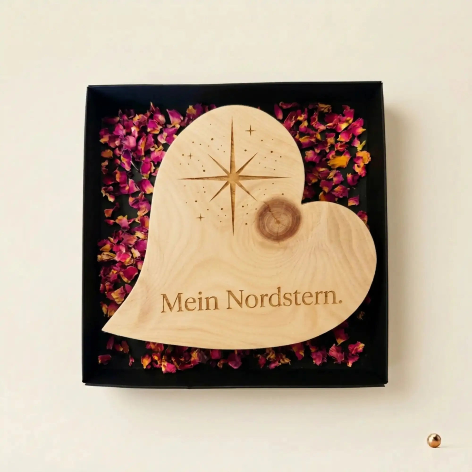 Zirbenholzherz mit Nordstern-Gravur und Schriftzug „Mein Nordstern“ in schwarzer Geschenkbox mit Rosenblueten als Dankeschoen zum Muttertag.