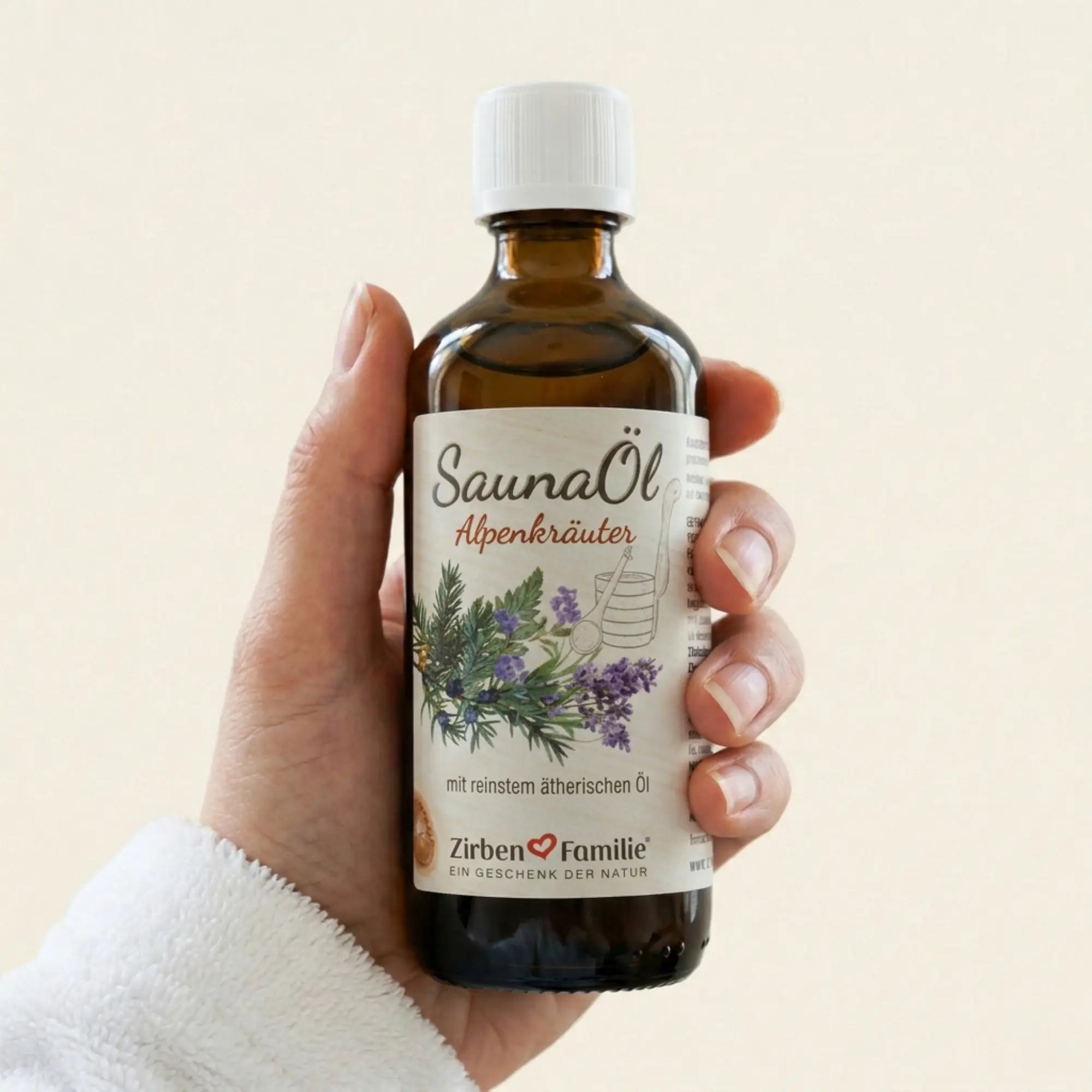 Hand haelt die 100ml Flasche Saunaoel Alpenkraeuter in einem hellen, freundlichen Spa-Ambiente vor strukturiertem Papierhintergrund. Hand haelt die 100ml Flasche Saunaoel Alpenkraeuter in einem hellen, freundlichen Spa-Ambiente vor strukturiertem Papierhintergrund.