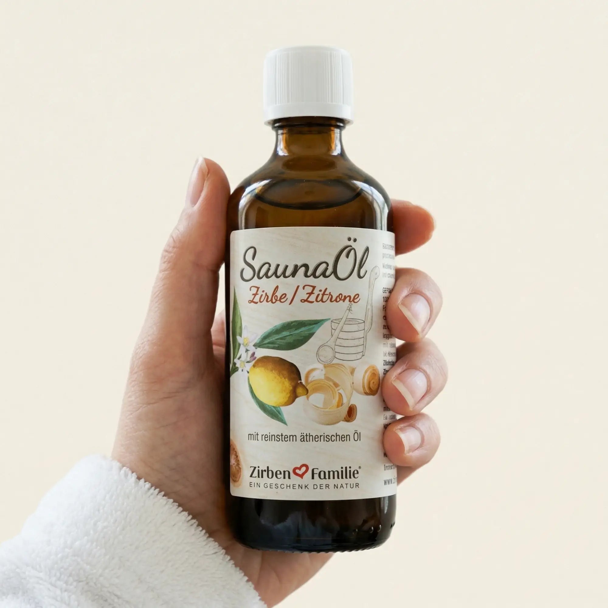 Hand haelt die 100ml Flasche Saunaoel Zirbe und Zitrone in einem hellen, freundlichen Spa-Ambiente vor hellem Hintergrund. Hand haelt die 100ml Flasche Saunaoel Zirbe und Zitrone in einem hellen, freundlichen Spa-Ambiente vor hellem Hintergrund.