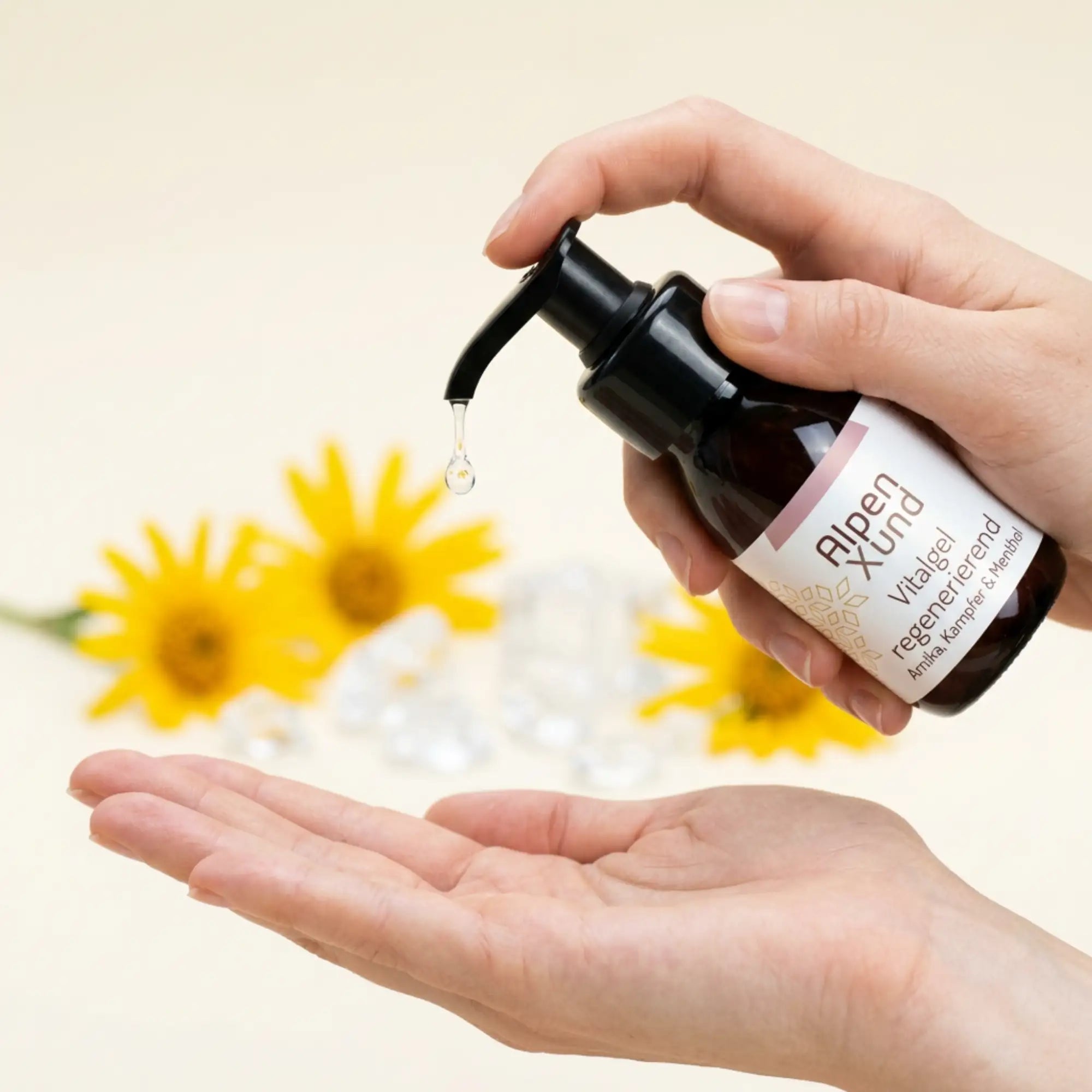 Kleiner transparenter Geltropfen faellt aus Vitalgel Flasche in Richtung Handflaeche. Arnika im Hintergrund. Kleiner transparenter Geltropfen faellt aus Vitalgel Flasche in Richtung Handflaeche. Arnika im Hintergrund.