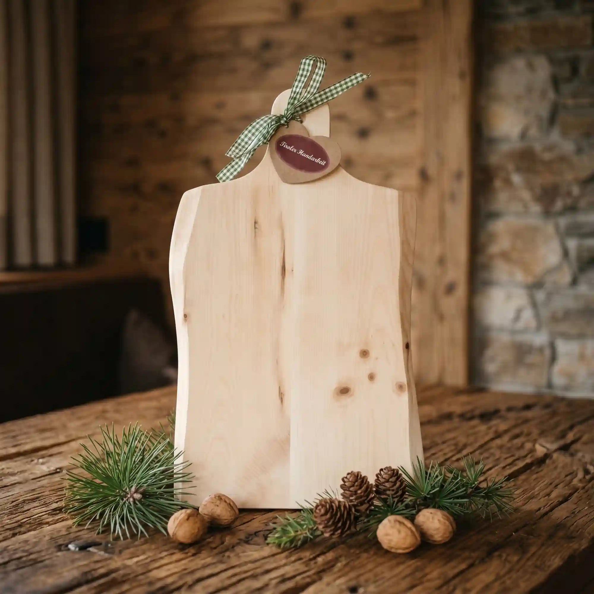 Massives Brotzeitbrett aus Zirbe mit gruen-weiss karierter Schleife im Landhausstil dekoriert mit Kiefernzweigen auf urigem Altholztisch.