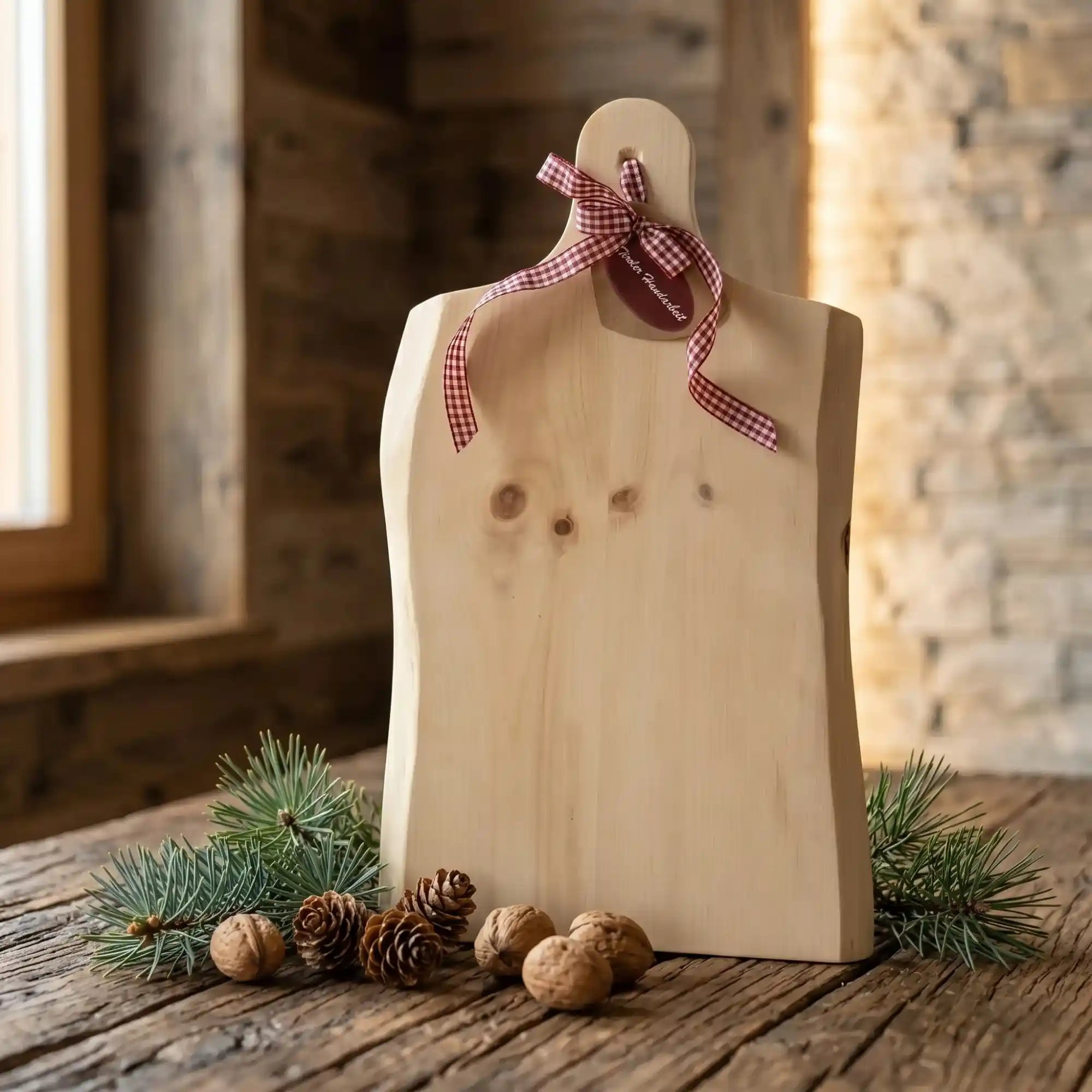 Rustikales XL Jausenbrett aus Zirbenholz mit rot-weiss karierter Schleife auf Holztisch mit Walnuessen und Tannenzapfen in einer Almhuette.