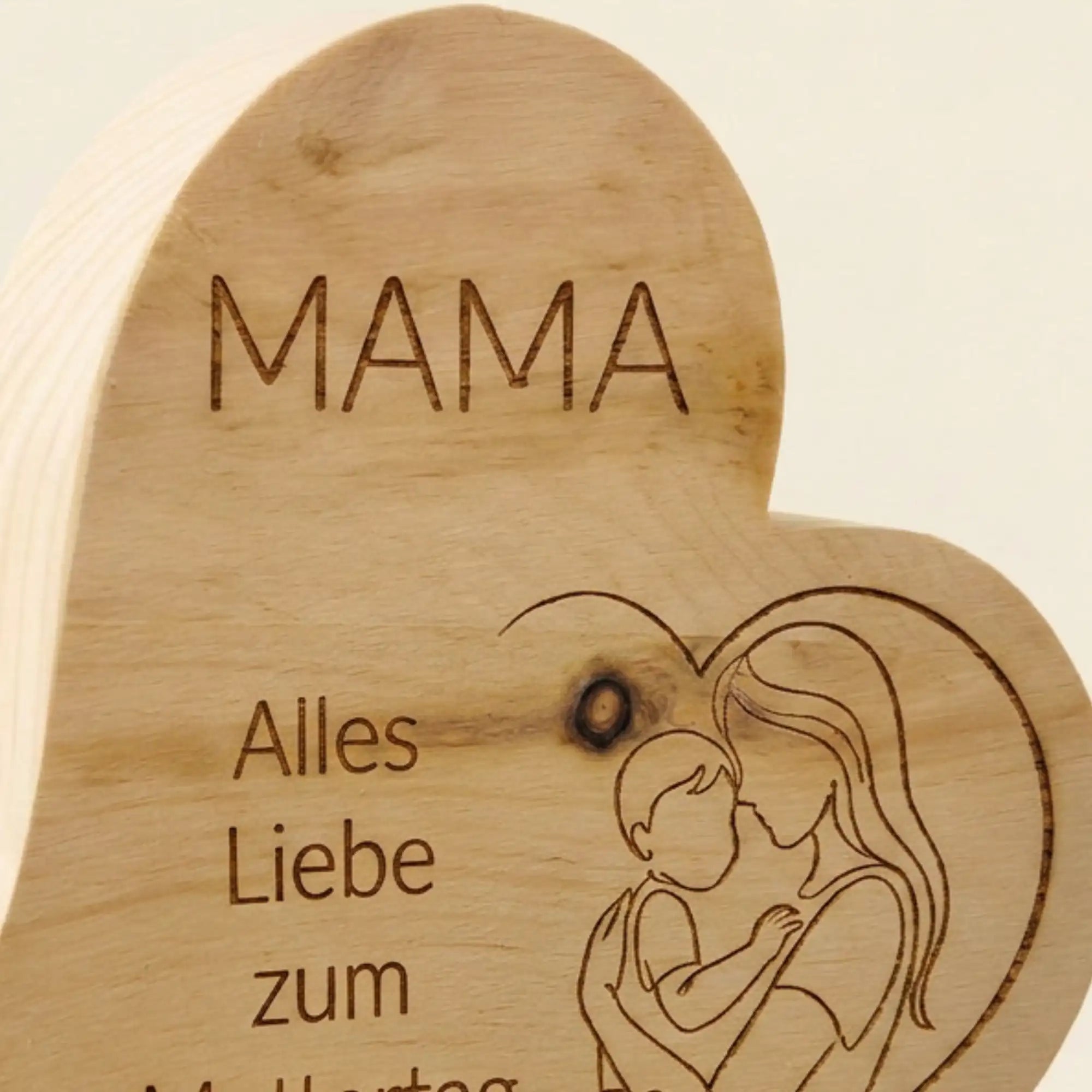 Nahaufnahme der praezisen Lasergravur Mutterliebe mit Mutter-Kind-Motiv auf dem Zirbenherz fuer das Muttertagsgeschenk 2026. Nahaufnahme der praezisen Lasergravur Mutterliebe mit Mutter-Kind-Motiv auf dem Zirbenherz fuer das Muttertagsgeschenk 2026.