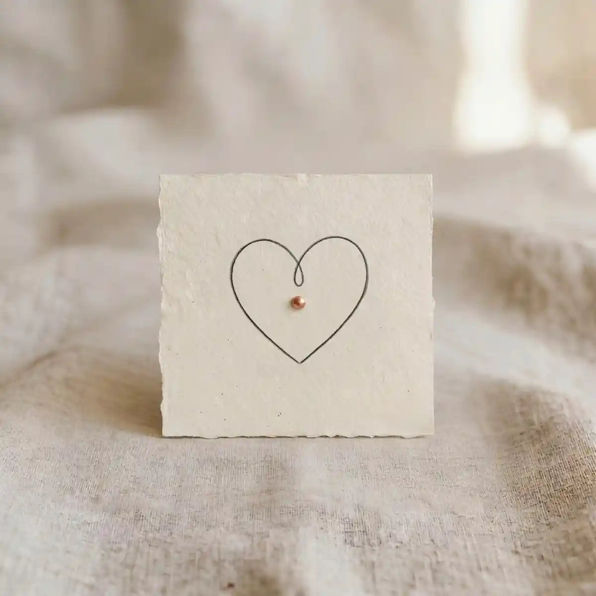 Minimalistische Single-Line-Herzzeichnung mit kupferfarbenem Akzent auf handgeschoepftem Papier.