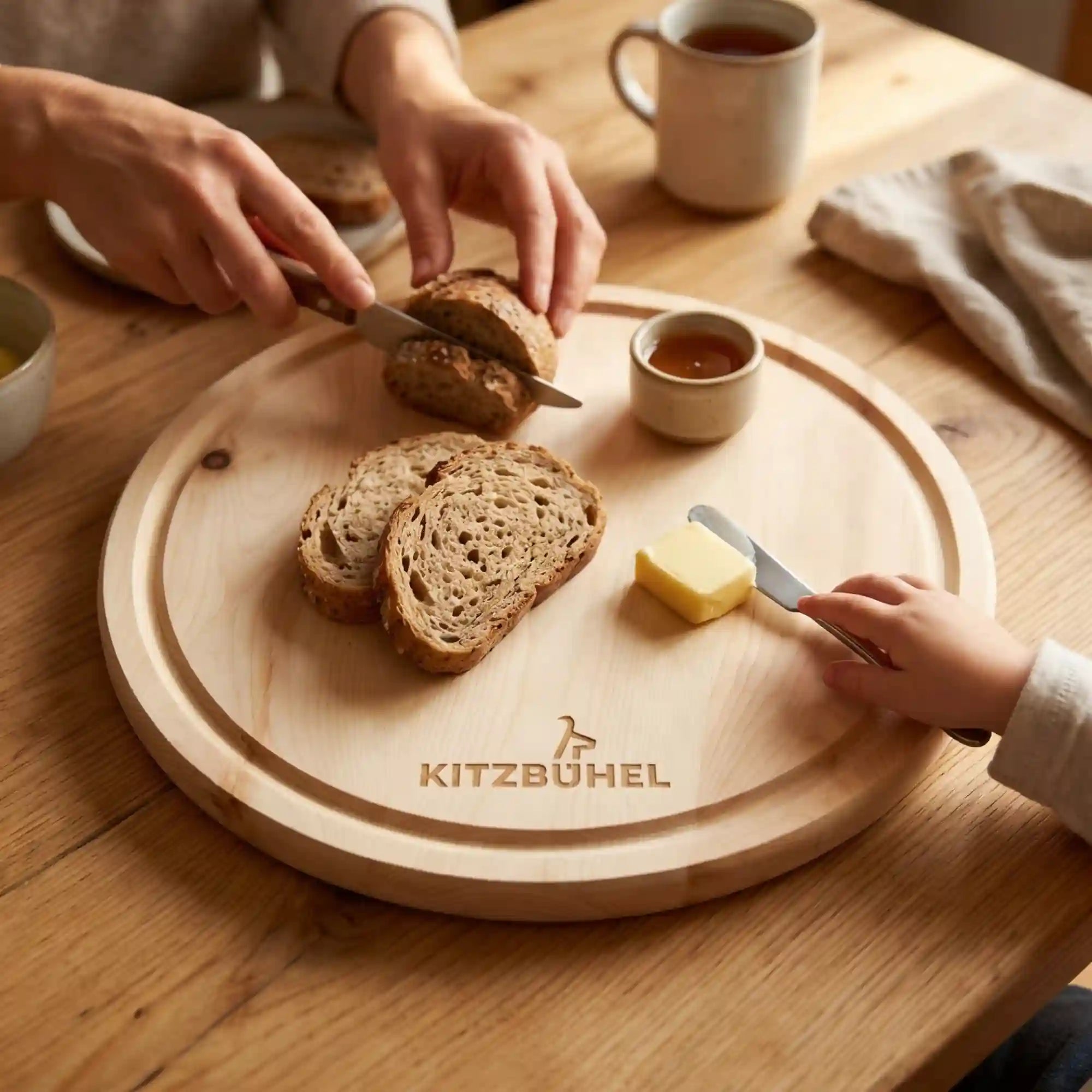 Makro-Foto: Rundes 25 cm Zirbenholz Jausenbrett mit Kitzbuehel Schriftzug, Semmel und Kinderhand beim Familienfruehstueck. Makro-Foto: Rundes 25 cm Zirbenholz Jausenbrett mit Kitzbuehel Schriftzug, Semmel und Kinderhand beim Familienfruehstueck.