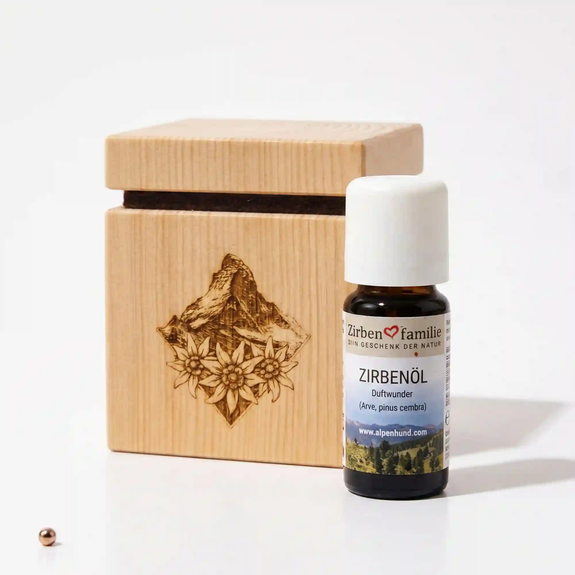 Zirbenquader Alpenblick aus massivem Zirbenholz mit Alpengipfel- und Edelweiss-Gravur neben einer 10ml Flasche Zirbenoel der ZirbenFamilie vor weißem Hintergrund.