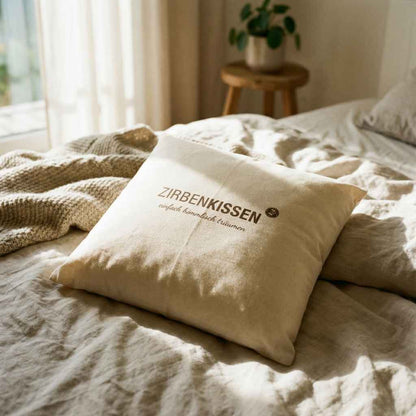 Zirbenprodukt ZirbenKissen 40x40cm “einfach himmlisch träumen” Zirbenprdukt liegt auf dem Bett, wird von Sonnenstrahlen erhellt, Helle bettdecke im Hintergrund pflanze