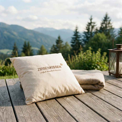 Zirbenprodukt ZirbenKissen 40x40cm “einfach himmlisch träumen”  auf einer Holzterasse im hintergrund wiesen berge und wald