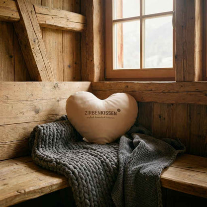 Zirben-Herzkissen beige natur Zirbenprodukt 40x40 cm mit natürlichen Zirbenflocken – handgefertigt in Tirol in einem Großen Lichtdurchfluteten Wohnzimmer auf einer Holzbank auf einer grauen gestrickten Decke