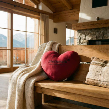 Rotes Zirben-Herzkissen Zirbenprodukt 40x40 cm mit natürlichen Zirbenflocken – handgefertigt in Tirol in einem Großen Lichtdurchfluteten Wohnzimmer auf einer Holzbank neben einer Beigen gestrickten Decke