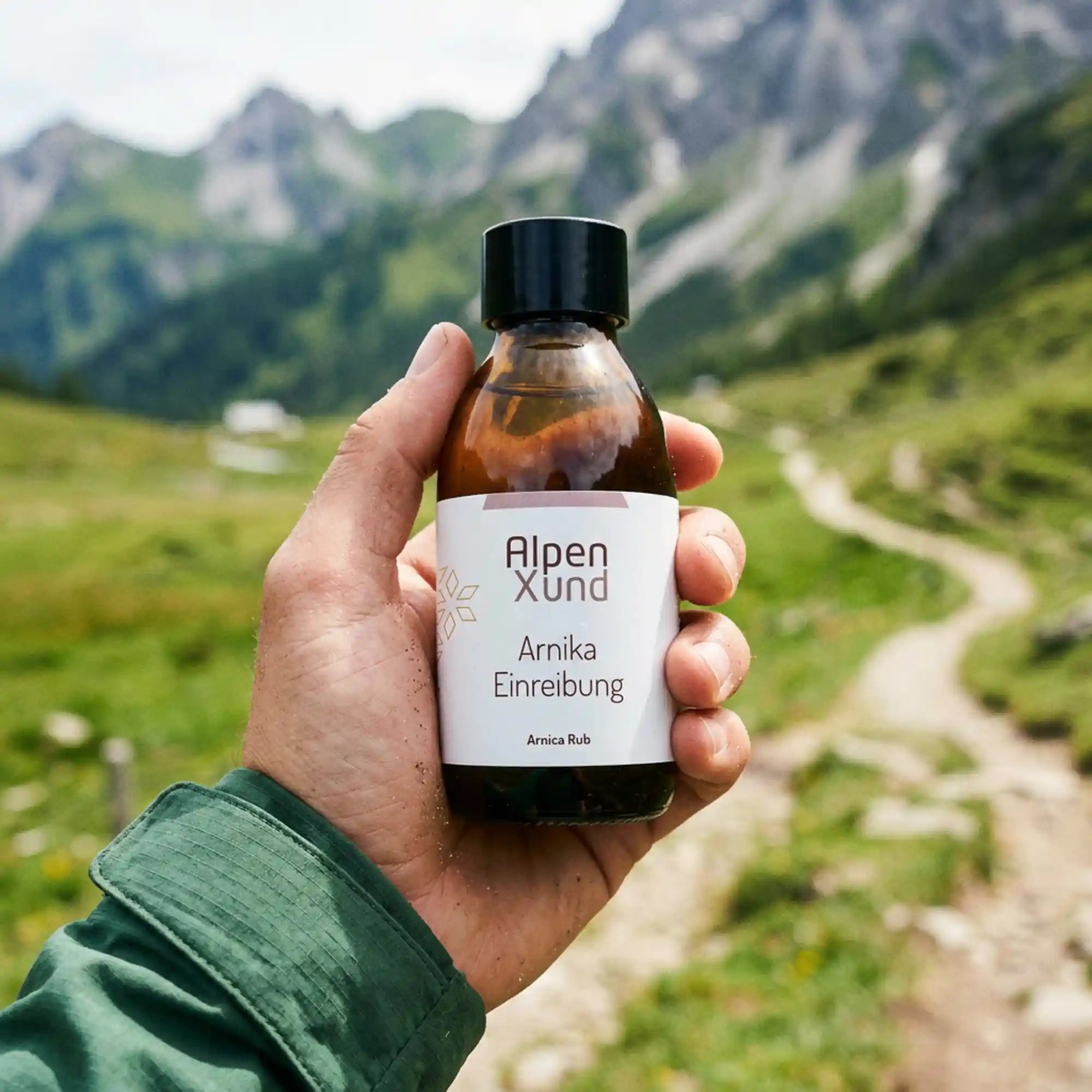Arnika Einreibung 150ml Flasche in einer Hand gehalten vor alpinem Hintergrund zum Groessenvergleich.