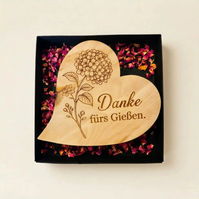 Graviertes Zirbenholzherz mit Hortensien-Motiv und Spruch „Danke fürs Gießen“ als Muttertagsgeschenk in einer offenen Box mit Rosenblueten.