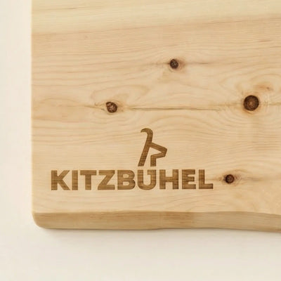 Detailansicht der lasergravierten Kitzbuehel-Schriftzug-Gravur auf einem Jausenbrett aus hellem Zirbenholz.