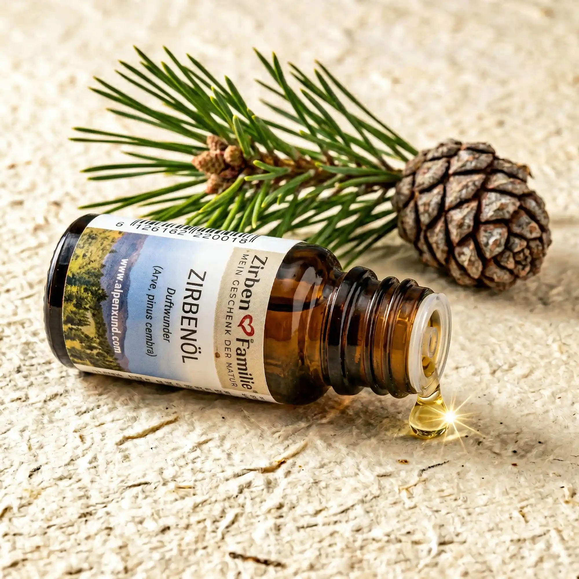 Liegende Zirbenoel Flasche mit goldenem Tropfen und Zirbenzweig auf Papier in beige, naturbelassenes Duftoel von GeschenkeReich.