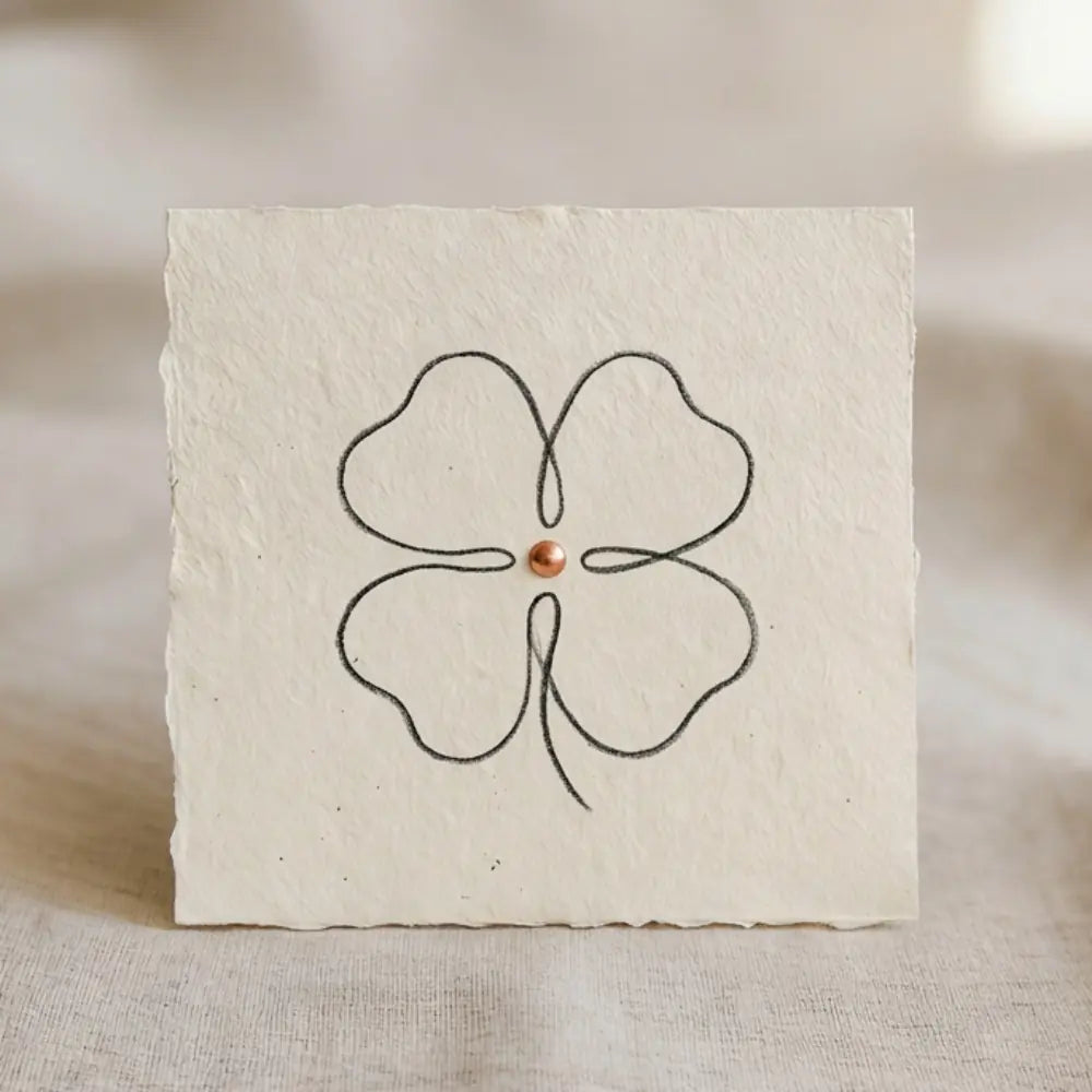 Fein gezeichnetes vierblaettriges Kleeblatt als minimalistische Liniengrafik auf hellem, strukturiertem Papier.