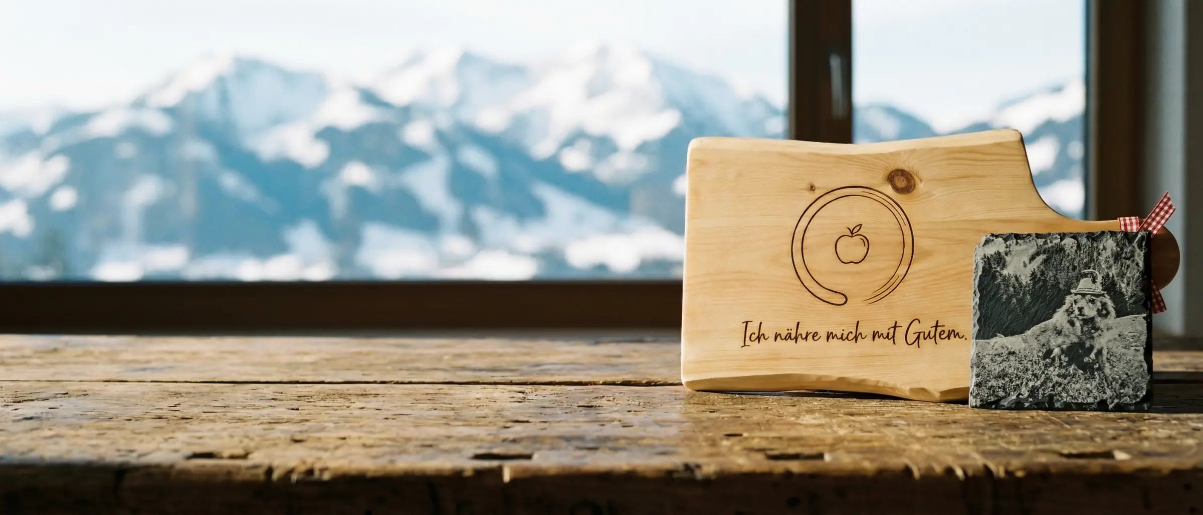 Gegenueberstellung von Fotogravur auf Pinus cembra und Symbolgravur auf Naturschiefer vor einem alpinen Bergpanorama - Manufaktur bei Kitz.