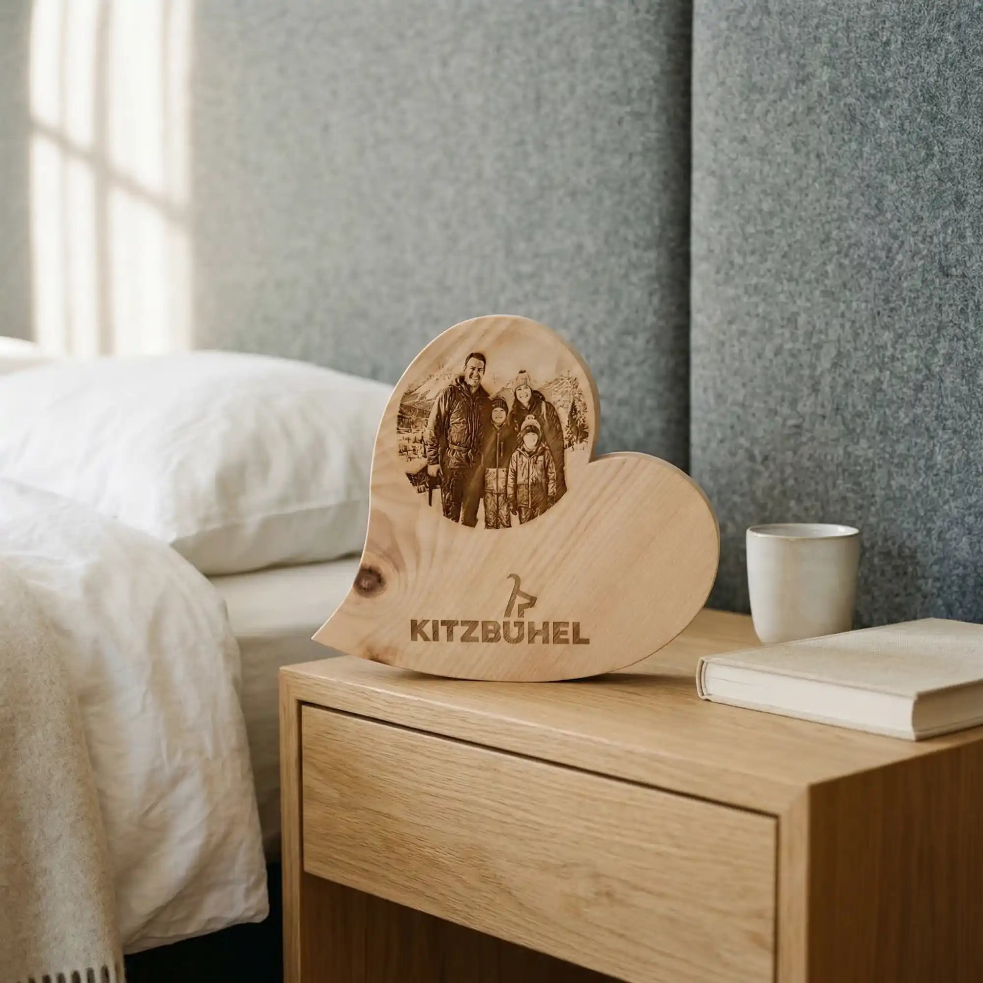 Personalisiertes Zirbenherz mit Kitzbuehel Schriftzug und Familienfoto als Deko auf einem Nachttisch im alpinen Schlafzimmer Design.