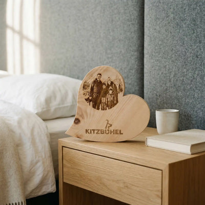 Personalisiertes Zirbenherz mit Kitzbuehel Schriftzug und Familienfoto als Deko auf einem Nachttisch im alpinen Schlafzimmer Design.