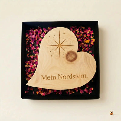 Zirbenholzherz mit Nordstern-Gravur und Schriftzug „Mein Nordstern“ in schwarzer Geschenkbox mit Rosenblueten als Dankeschoen zum Muttertag.