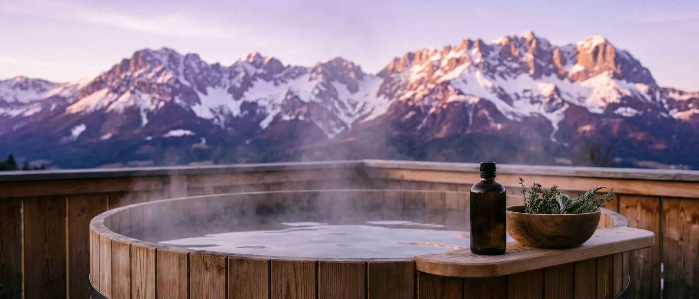 Dampfender Badezuber auf einer Laerchenholz-Terrasse in Kitzbuehel mit Blick auf den Wilden Kaiser bei Sonnenuntergang, dekoriert mit Bio-Zirbenoel und alpiner Naturkosmetik.