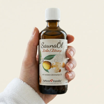 Hand haelt die 100ml Flasche Saunaoel Zirbe und Zitrone in einem hellen, freundlichen Spa-Ambiente vor hellem Hintergrund.