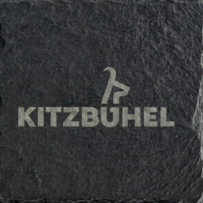 Nahaufnahme eines Schiefer Untersetzers mit grosser, lizenzierter Kitzbuehel Schriftzug Gravur auf dunklem Naturstein.