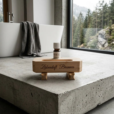 Zirbenduft-Brunnen auf Sichtbeton vor einem Fenster mit Wald- und Bergblick in einem modernen Loft.