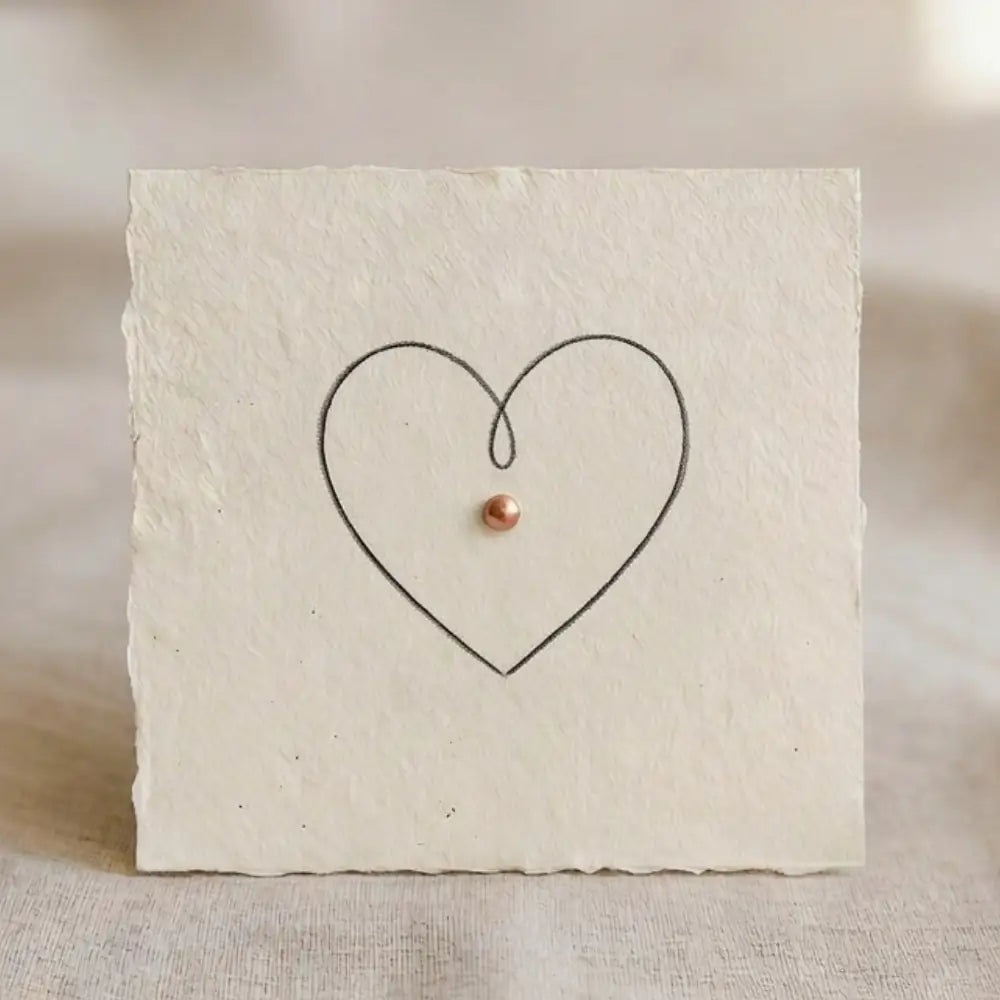 Minimalistische Single-Line-Herzzeichnung mit kupferfarbenem Akzent auf handgeschoepftem Papier.