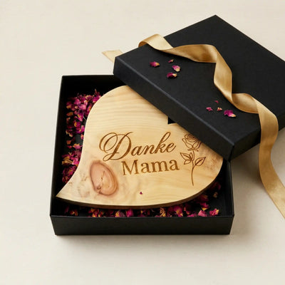  Zirbenholzherz Danke Mama in geoeffneter Geschenkbox mit goldener Schleife und getrockneten Blueten als Muttertagsgeschenk.