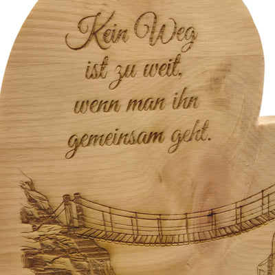 Detailaufnahme der Gravur mit Haengebruecke zwischen zwei Felsen auf Zirbenherz aus Holz mit sichtbarer Maserung.