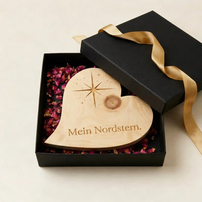 Zirbenholzherz mit Nordstern-Gravur und Schriftzug „Mein Nordstern“ in schwarzer Geschenkbox mit Rosenblueten als Dankeschoen zum Muttertag.