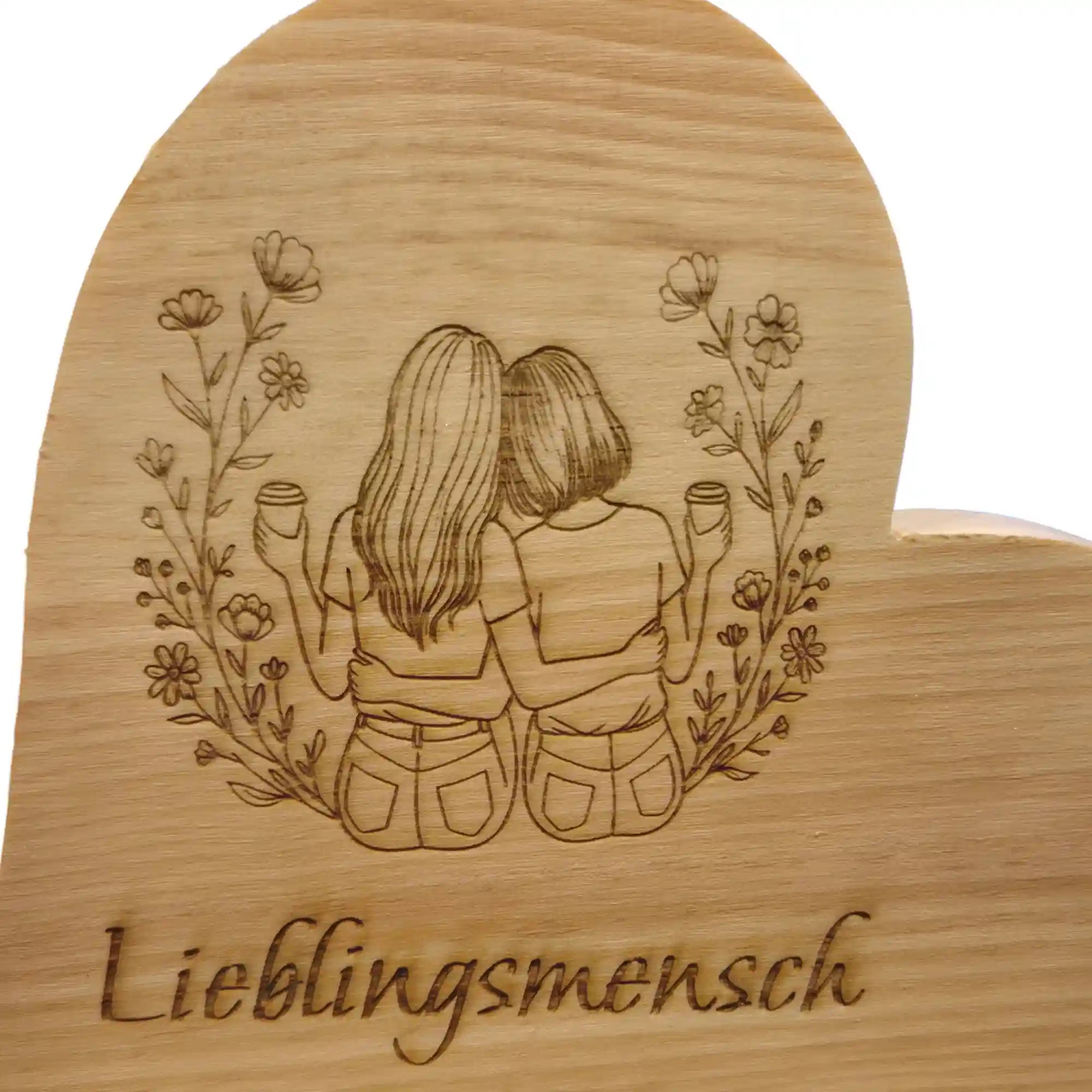 Detailaufnahme der Gravur mit zwei nebeneinander sitzenden Personen und Blumen auf Zirbenherz aus Holz mit sichtbarer Maserung.