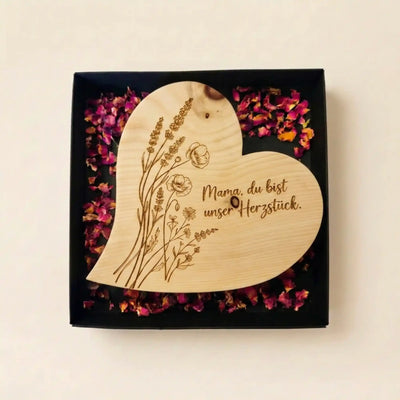 Geoeffnete schwarze Geschenkbox zum Muttertag 2026 mit Zirbenherz Mama, du bist unser Herzstueck auf duftenden Rosenblueten.