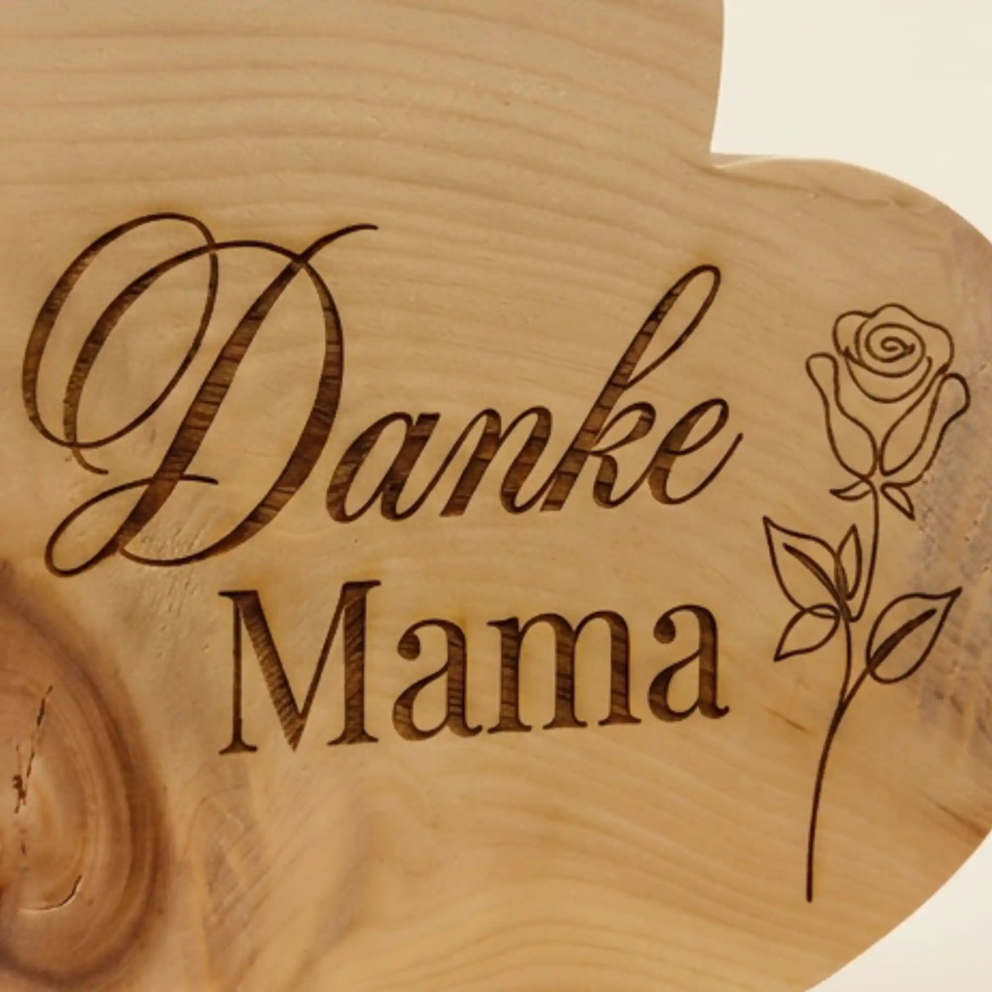 Detailaufnahme der 'Danke Mama' Gravur mit Rose auf einem Zirbenherz aus massivem Naturholz, hochwertiges Muttertagsgeschenk mit feiner Linienfuehrung.