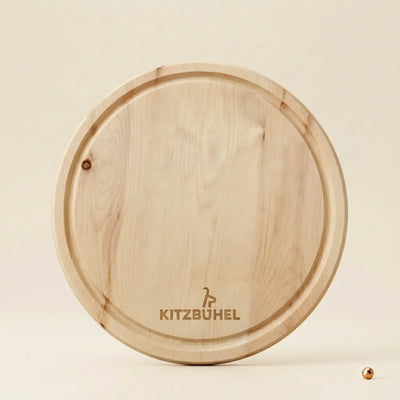 Rundes Jausenbrett aus massivem Tiroler Zirbenholz mit offizieller Kitzbuehel Lizenzgravur, Durchmesser 25 cm, auf neutralem Hintergrund.