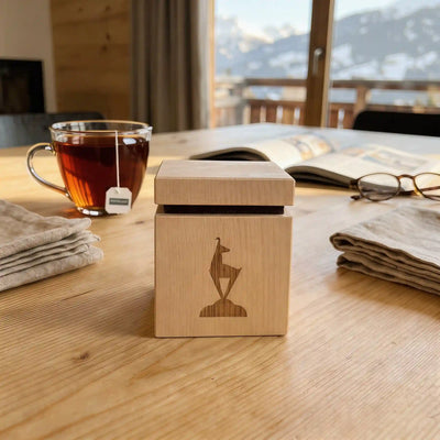 Zirbenwuerfel mit Gams Gravur auf hellem Holztisch neben dampfender Teetasse im Chalet.